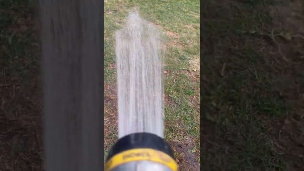 Water sprays from a hose nozzle onto a grassy lawn, demonstrating the watering process.