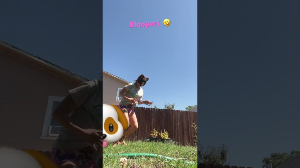 A person wearing a mask and casual clothes playfully dances outside in a backyard with a wooden fence. The word "Bloopers" and a laughing emoji appear at the top. A dog face emoji partially covers the left side.