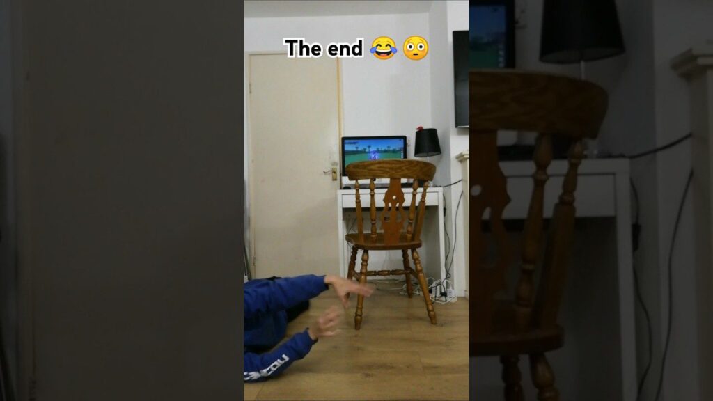 Person lying on the floor pointing at a wooden chair in front of a computer screen. The text "The end 😂😳" is visible above. A lamp and white desk are in the background.